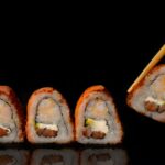 Cztery kawałki sushi na czarnym tle i patyczki, które chwytają jedną sztukę